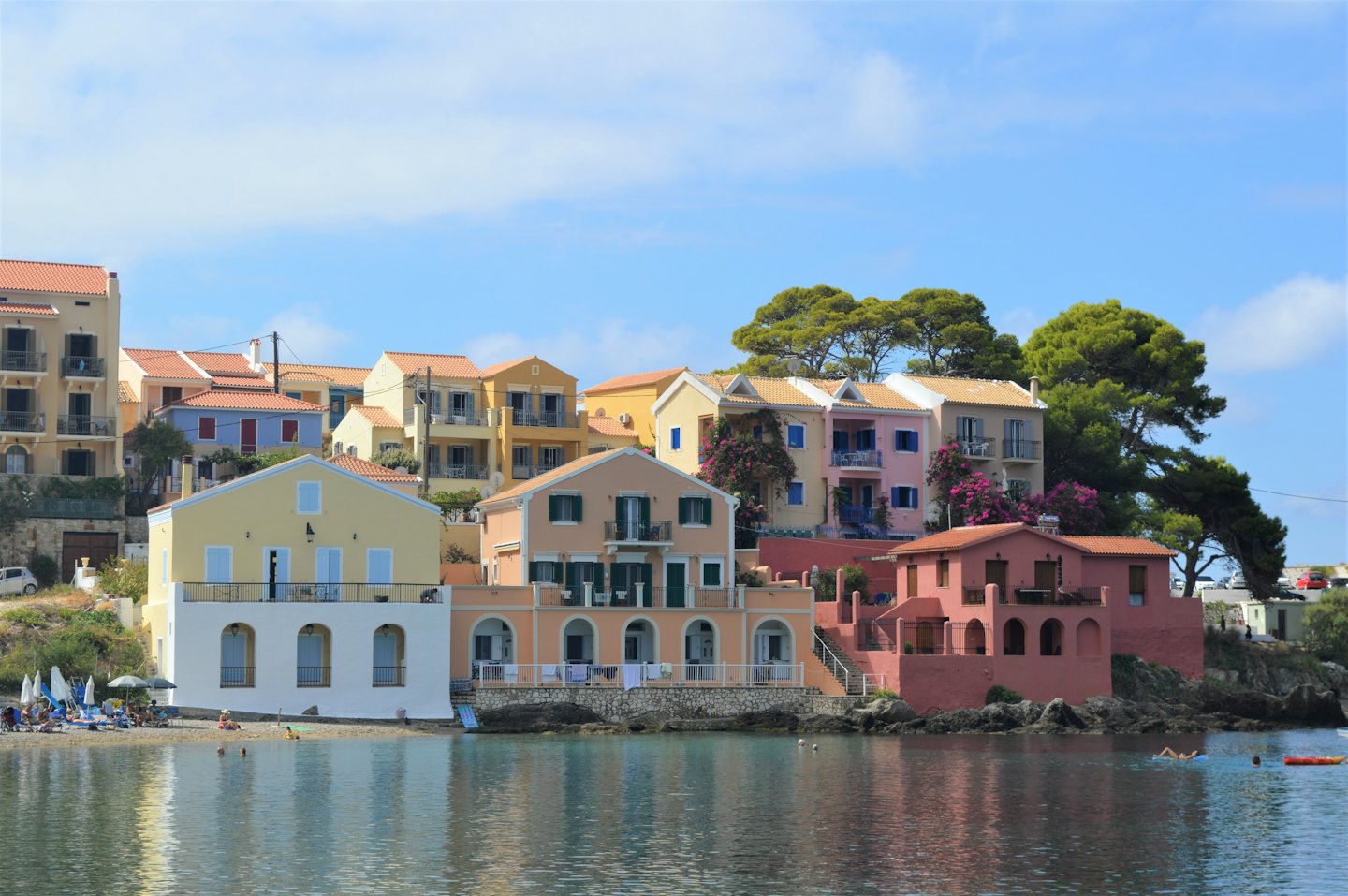 Case colorate di un villaggio mediterraneo che si affacciano su una spiaggia di ciottoli soleggiata.