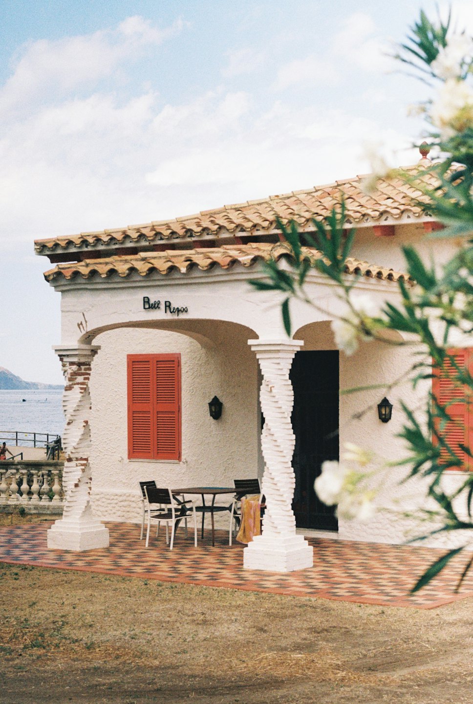 Casa mediterranea con persiane rosse affacciata sul mare calmo.